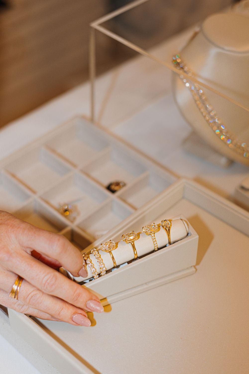 A hand displaying gold rings on a jewelry tray beside a sparkling necklace display in a boutique.