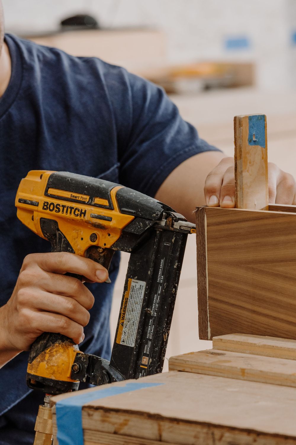Yellow Bostitch nail gun being used to attach wooden pieces in construction.