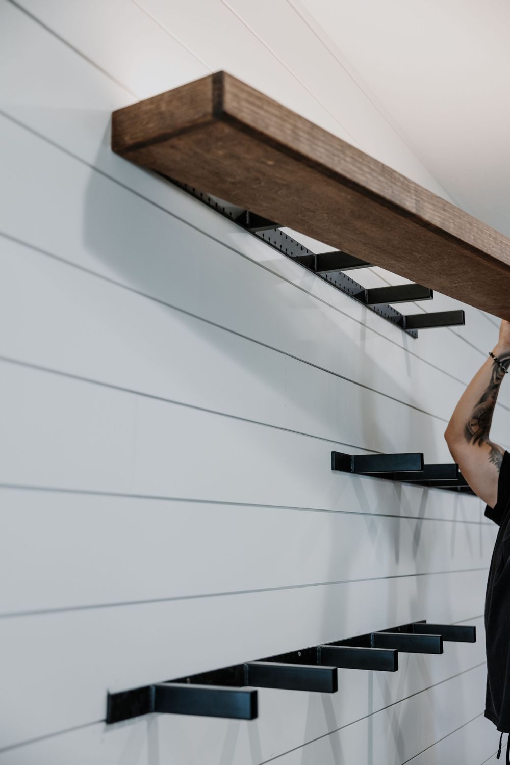 Installation of floating wooden shelves on white shiplap wall showing mounting brackets.