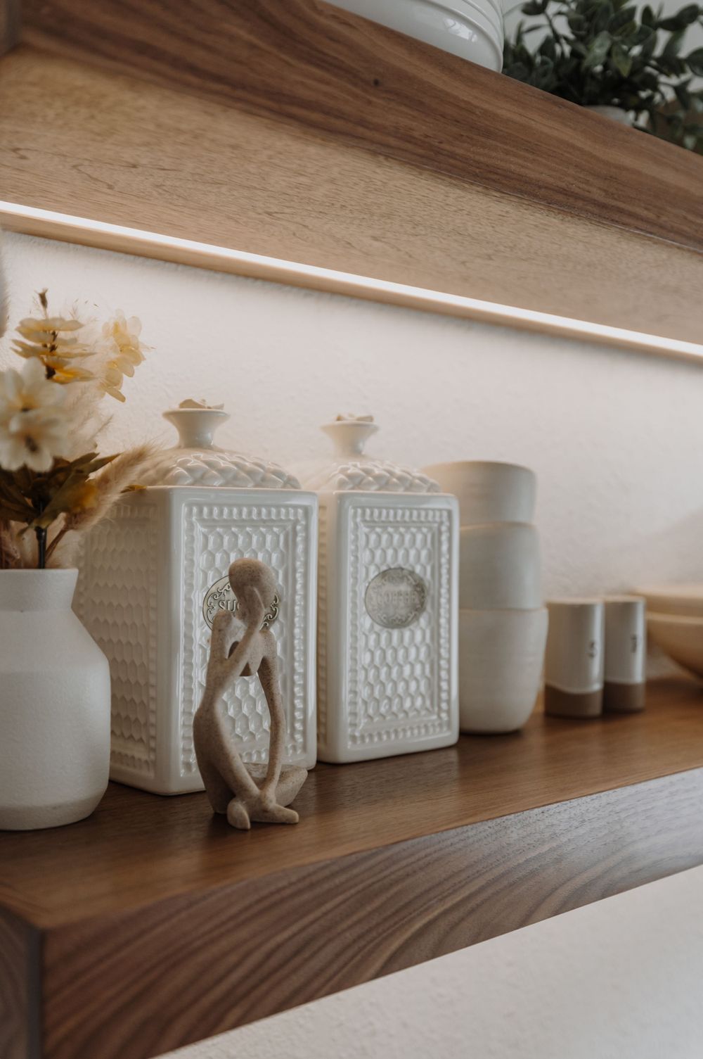 White decorative ceramic containers arranged on a wooden shelf.
