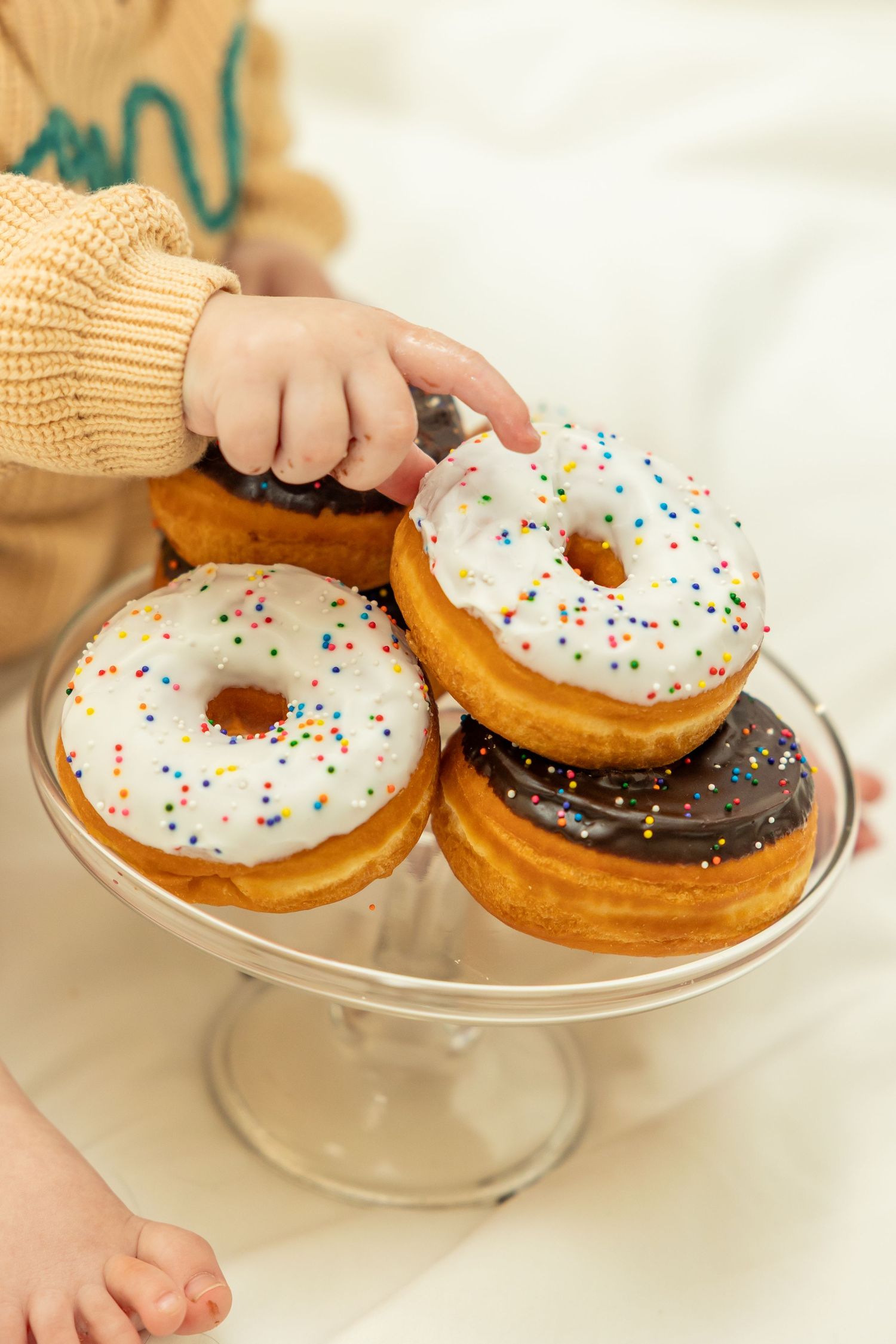 Frosted donuts with colorful sprinkles displayed on a glass cake stand (Kenansville, NC).