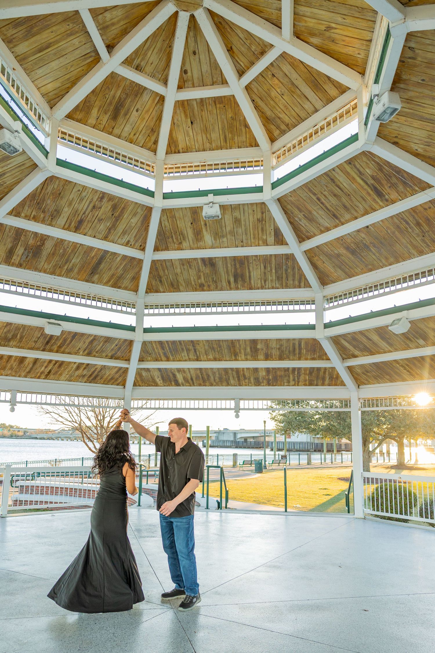 Couple stands in an octagonal wooden gazebo during golden hour (New Bern, NC).