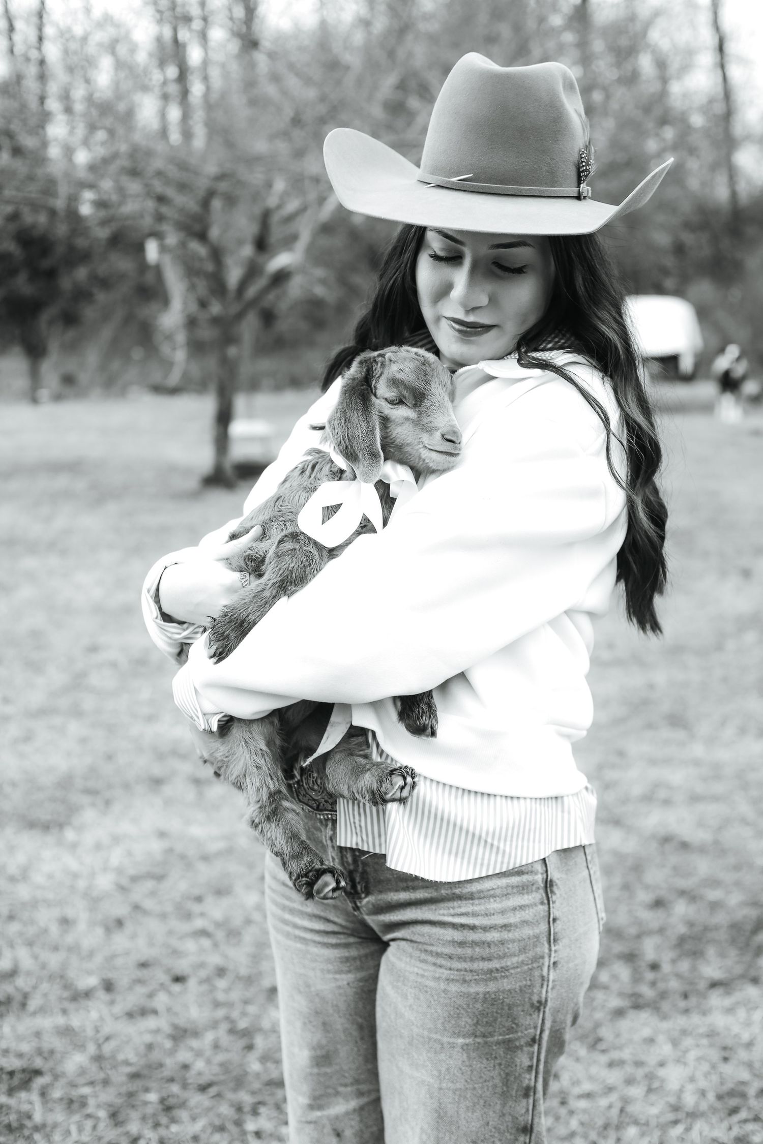 Black and white series showing someone in jeans and cowboy hat holding a small farm animal in a rustic outdoor setting (Beulaville, NC).