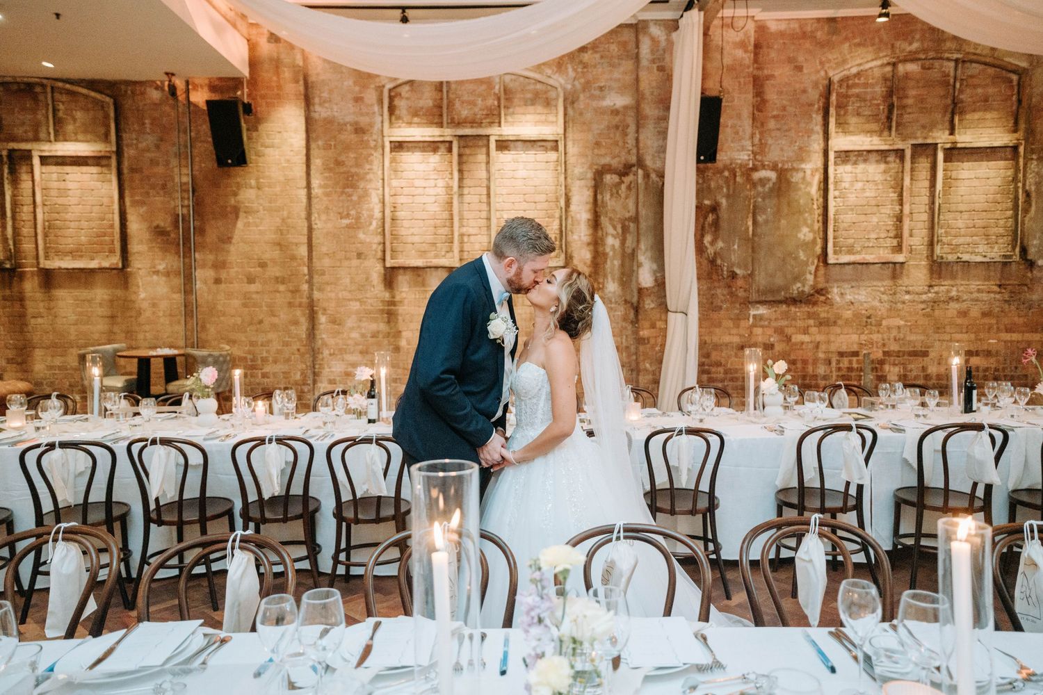 Wedding reception setup in a rustic venue with exposed brick walls and elegant table settings.