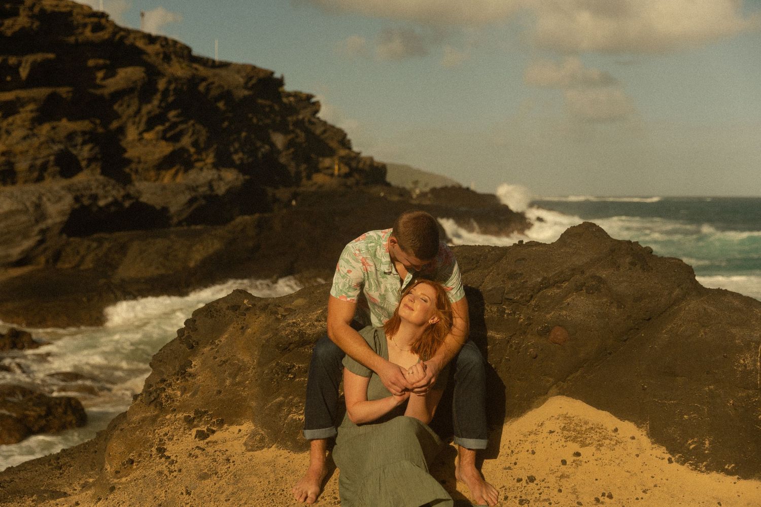 Couple shares intimate moment on rocky ocean cliff during sunset.