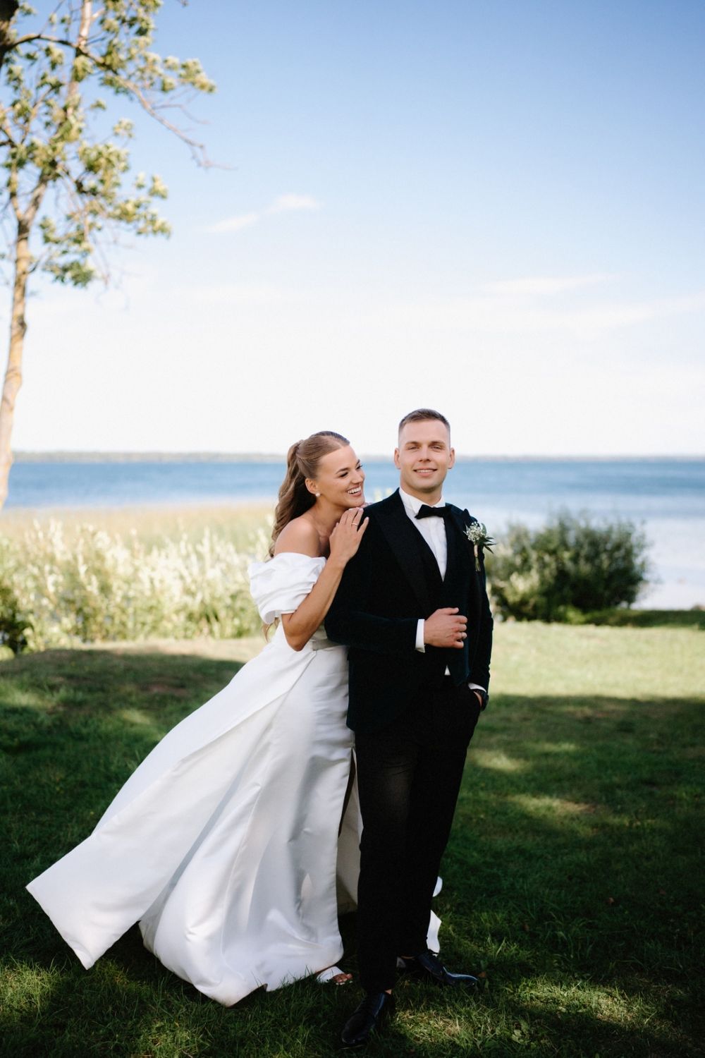 Elegant wedding couple laughing together by a lakeside on their special day.