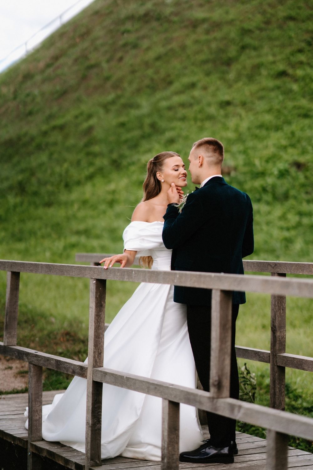 Wedding couple sharing an intimate moment on a rustic wooden bridge surrounded by green hills.