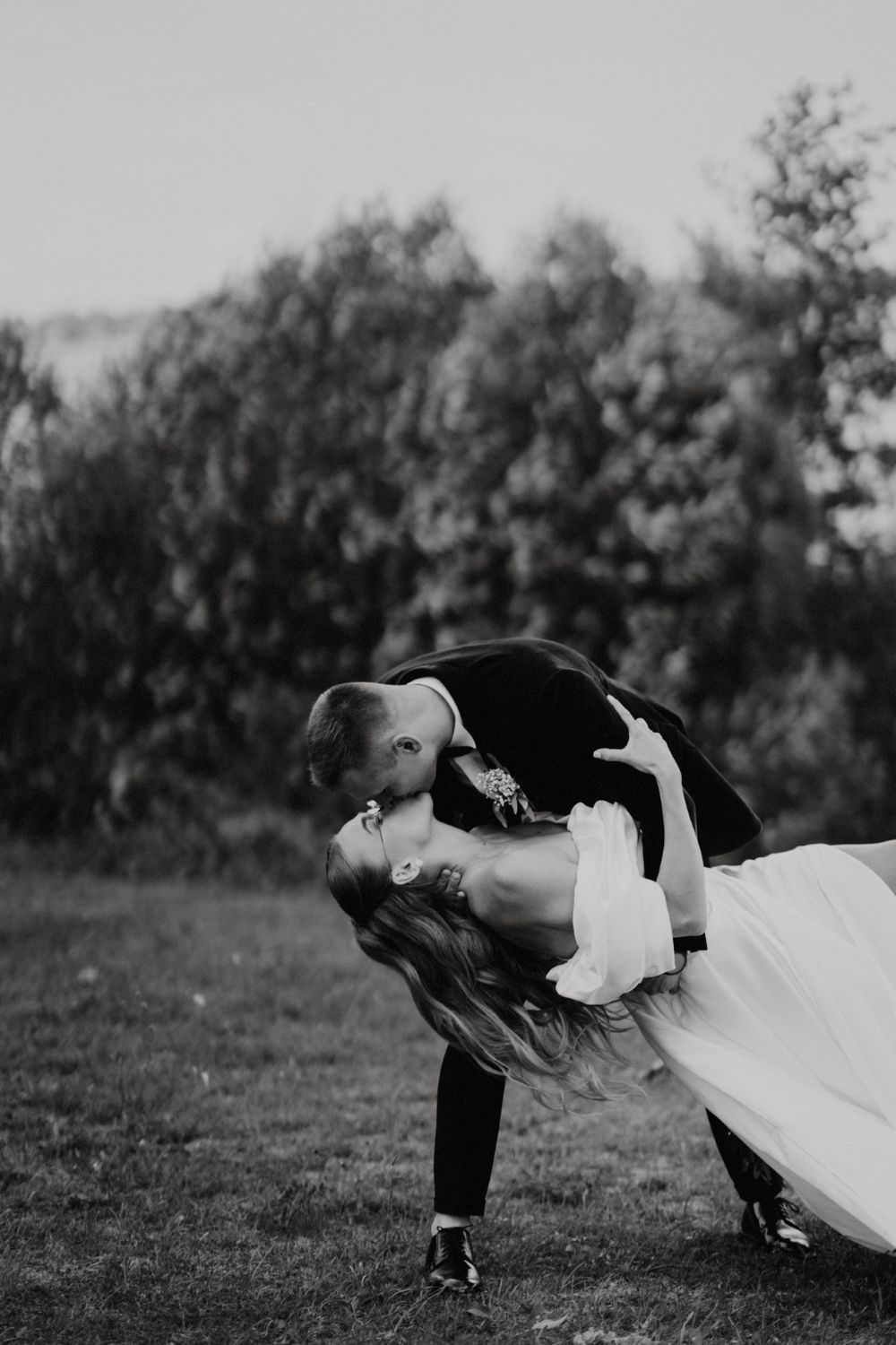 Dramatic black and white wedding dance dip pose in a natural outdoor setting.
