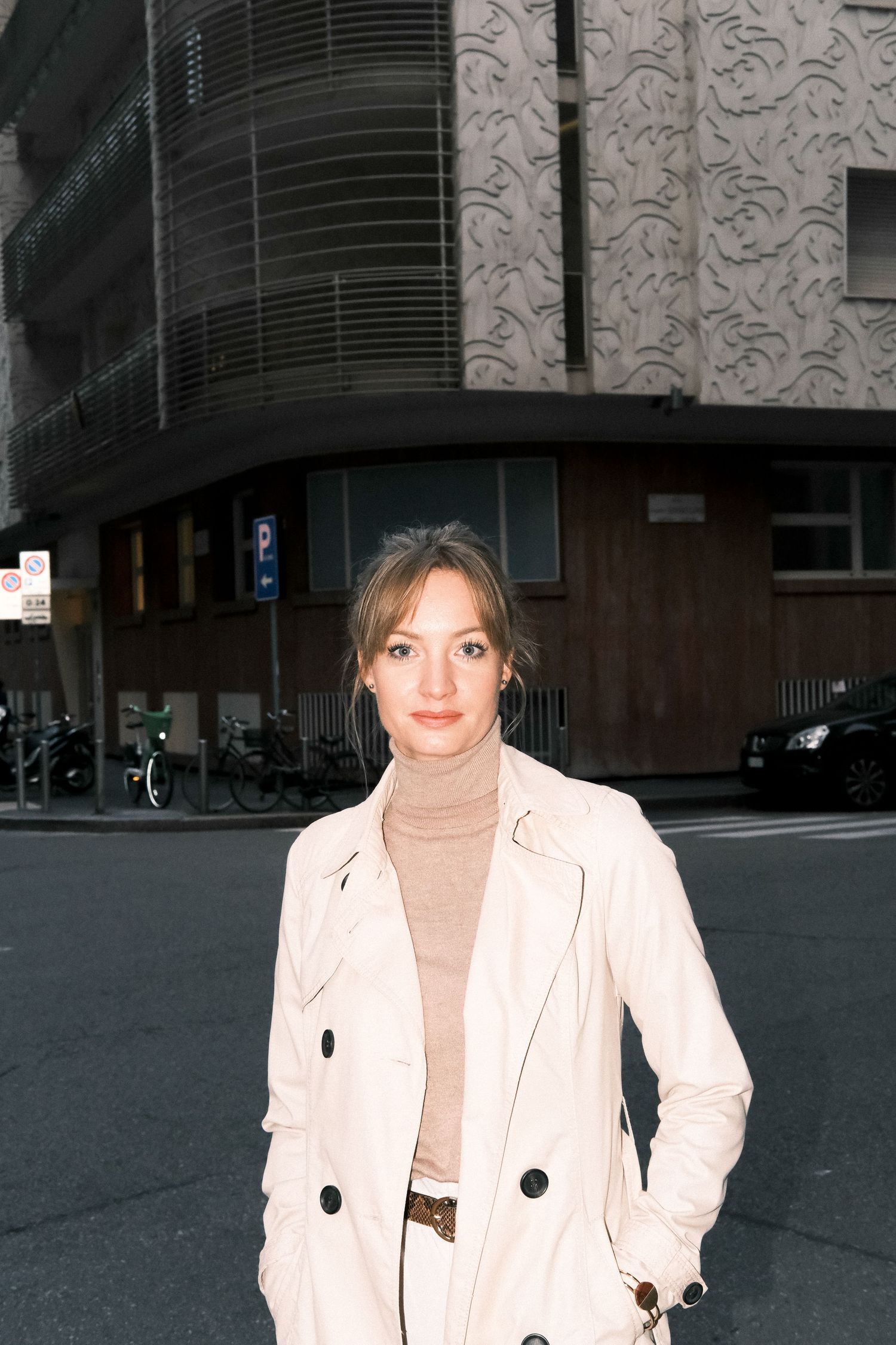 A woman in a beige trench coat on a city street.