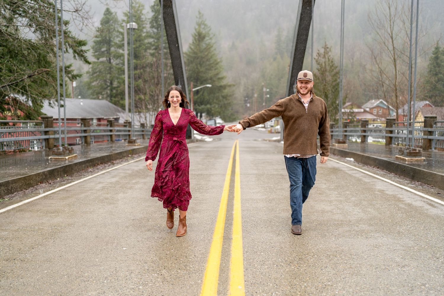 A couple joyfully runs hand in hand across a misty bridge in the Pacific Northwest wilderness.