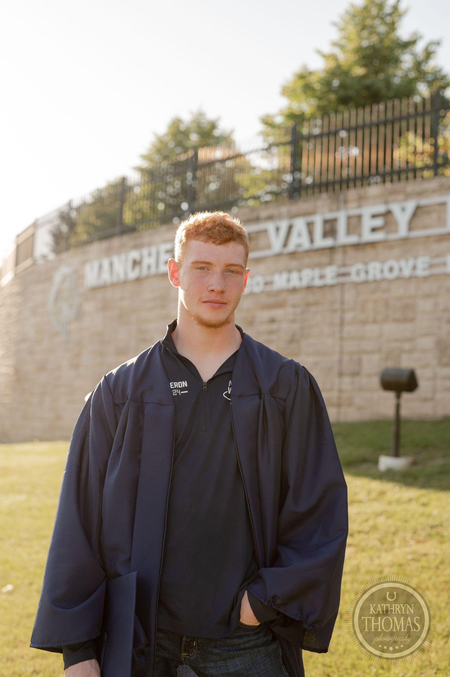 Student stands in graduation attire near Manchester Valley High School sign.