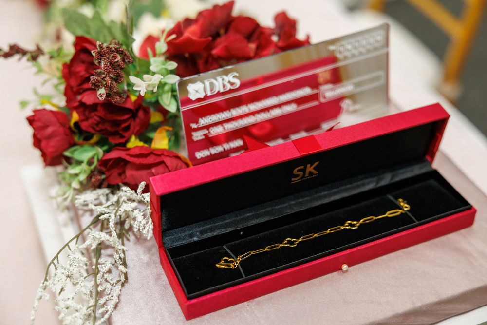 Red jewelry box with gold accents displayed among red roses and floral decorations.