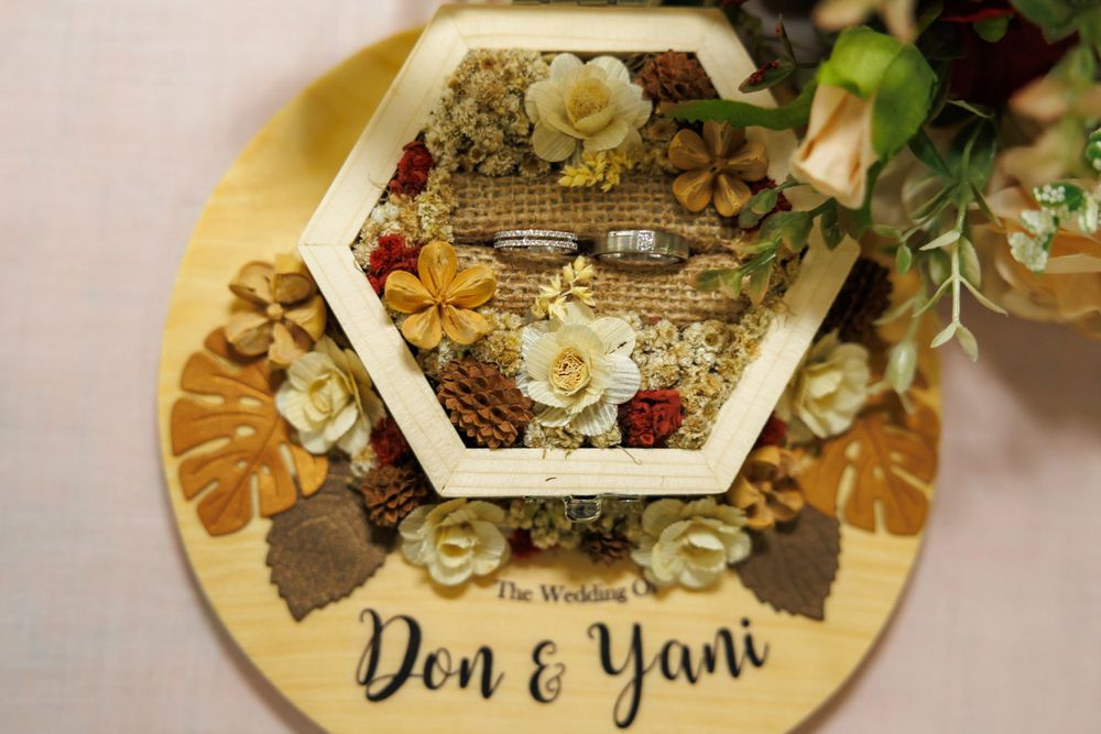 Hexagonal ring holder with "Don & Yani" text decorated with dried flowers and personal touches.