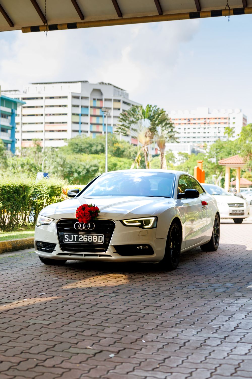 White Audi A5 decorated with red flowers parked on brick pavement with apartment buildings in background.