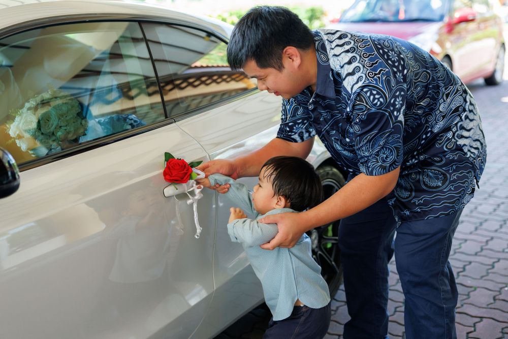 Person attaching floral decorations to white car door handle during wedding preparations.