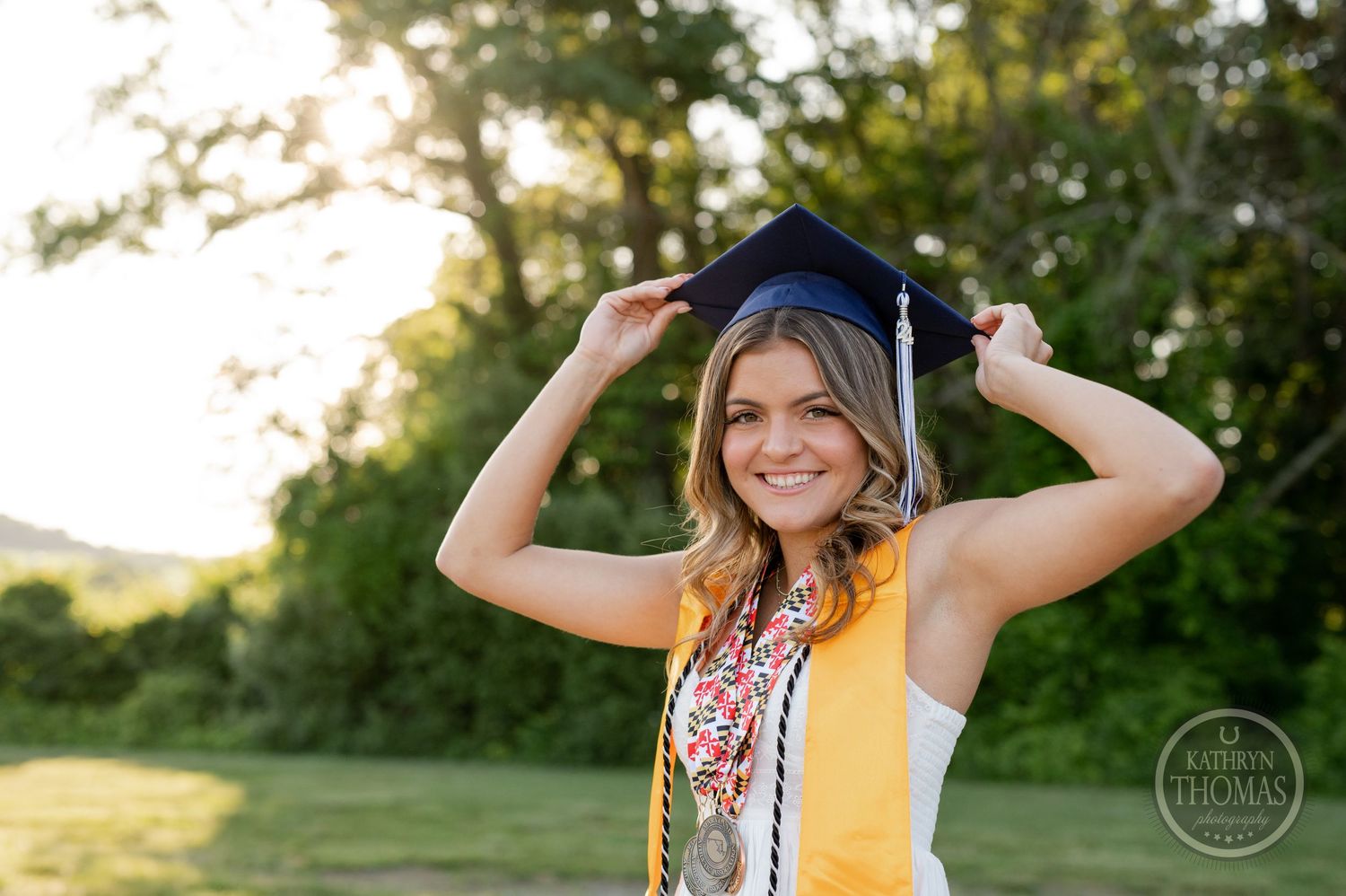 Graduate in academic attire playfully adjusts cap while posing outdoors.