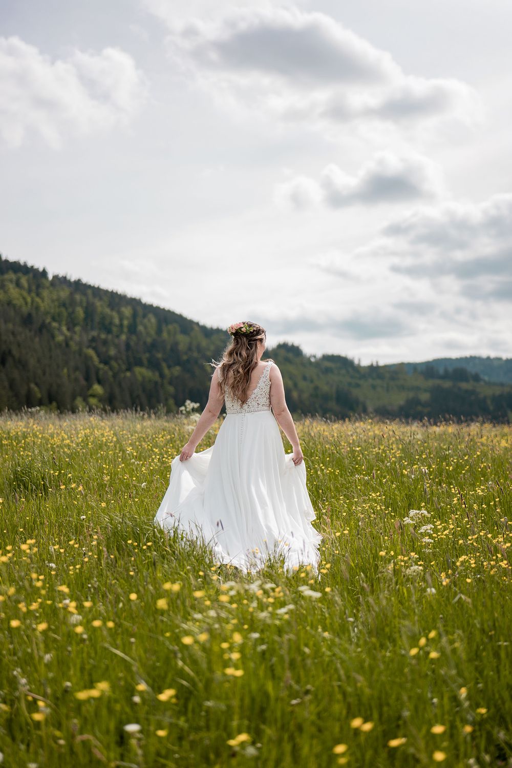 Die Braut läuft allein durch eine weite Wildblumenwiese in Richtung der bewaldeten Schwarzwaldberge bei Hinterzarten