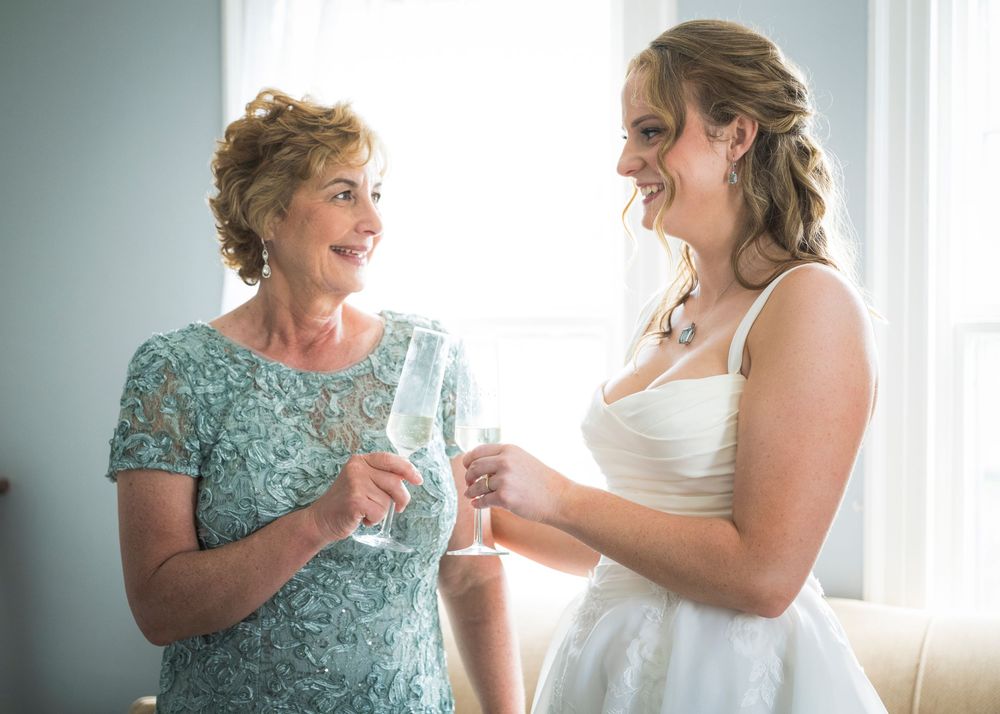 Bride in white wedding dress toasting champagne with an older woman in a teal lace dress.