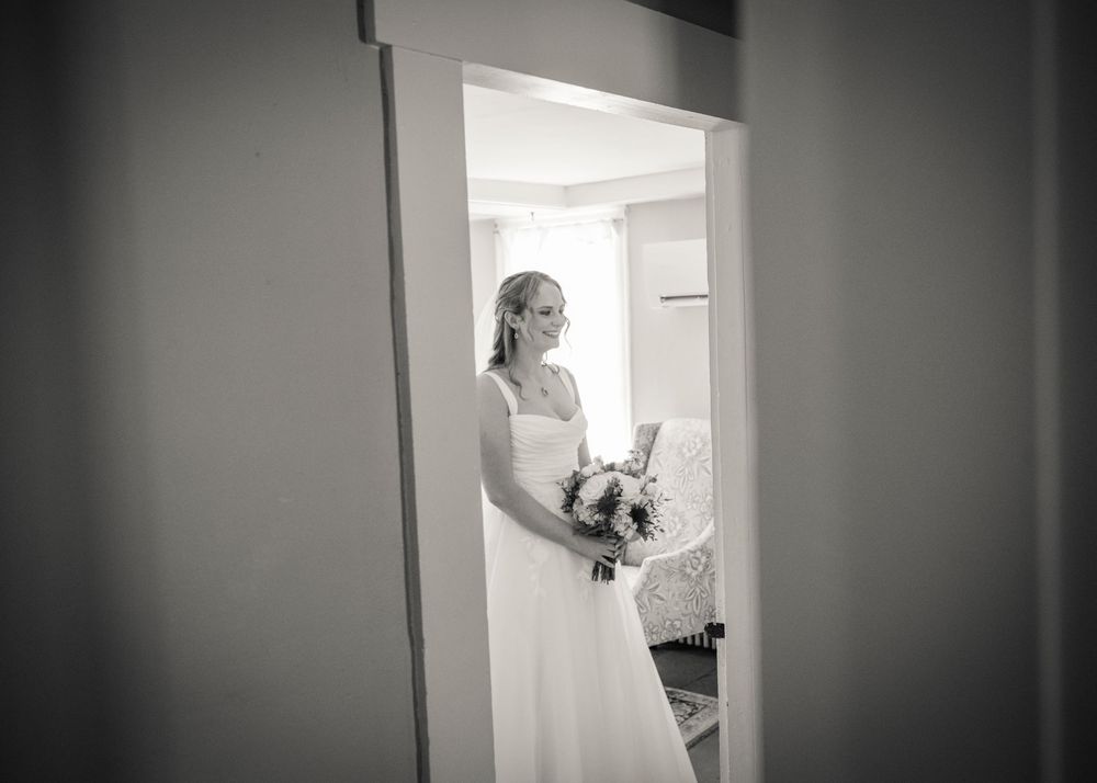 Black and white portrait of a bride holding a bouquet, framed in a doorway before her wedding.