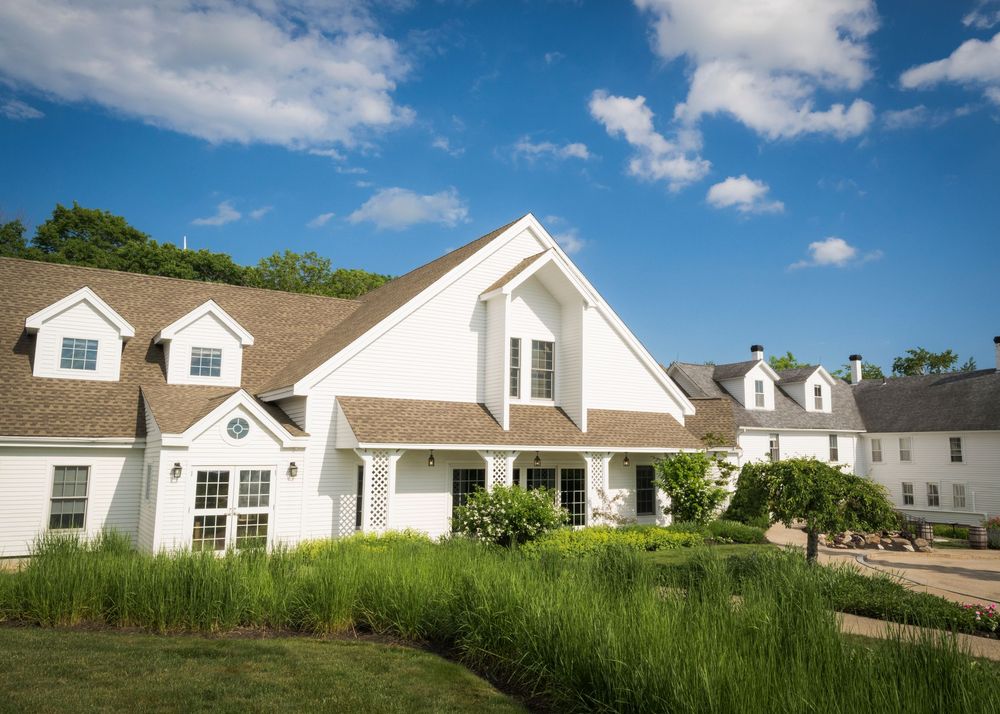 Elegant white wedding venue with dormer windows, manicured hedges, and blue sky with fluffy clouds.