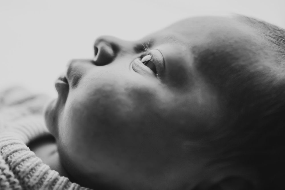 A black and white close-up photo of a person sleeping peacefully on white bedding.