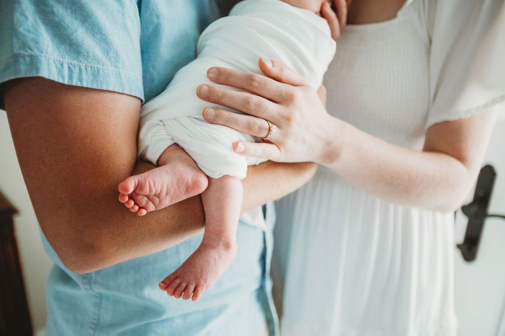 Parents gazing lovingly at their newborn baby's feet in a tender moment at home.