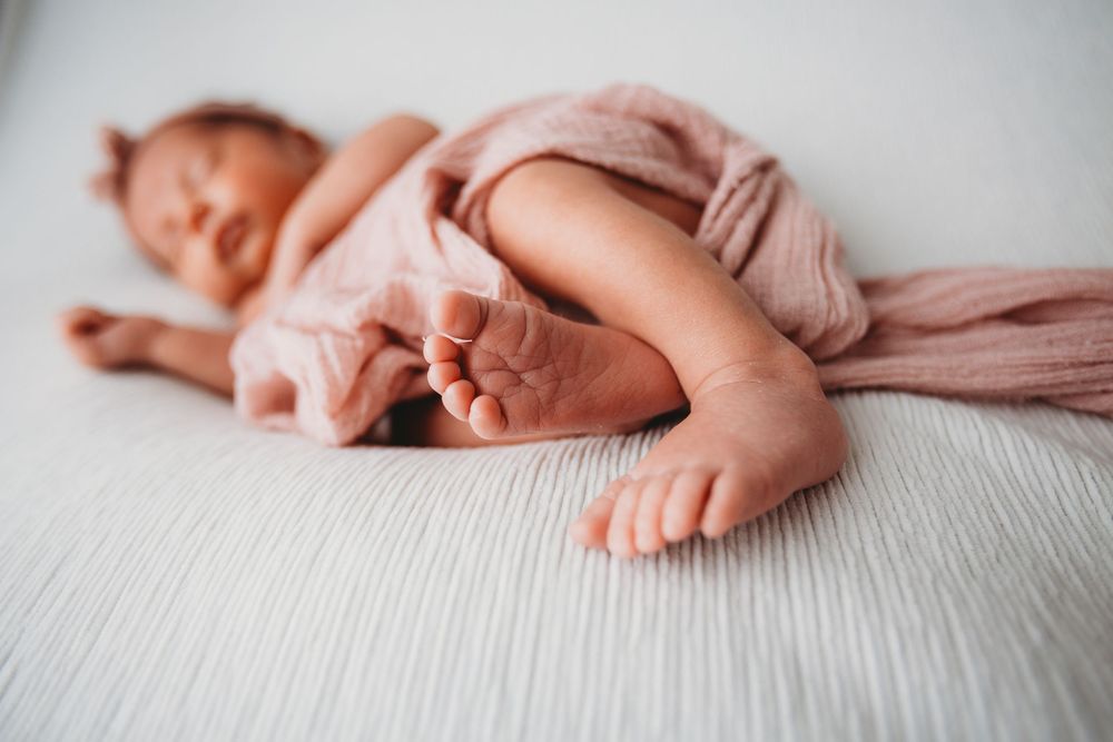 Delicate newborn baby feet and hands resting on soft white textured bedding in a series of artistic close-up shots.