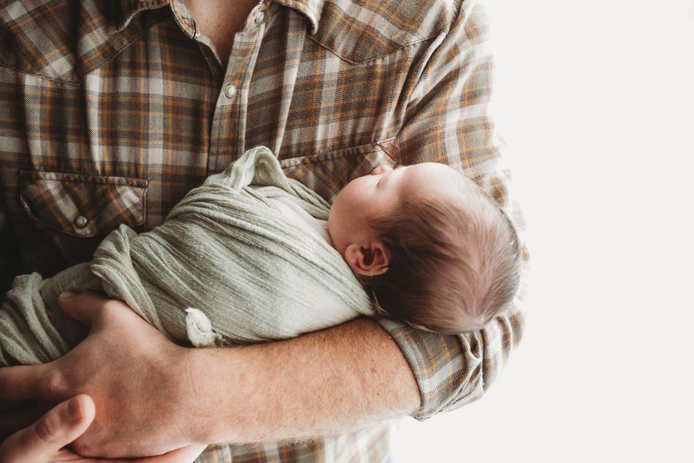 A person in a plaid shirt holds and comforts a crying newborn baby.
