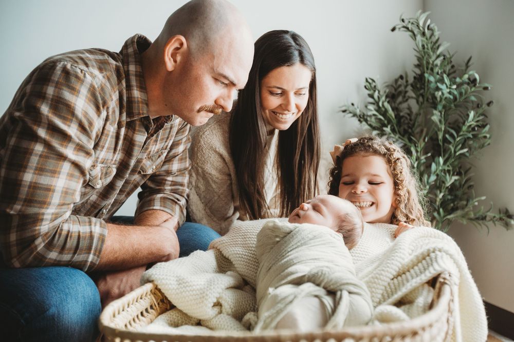 A family shares a joyful moment together while relaxing on a couch with a cozy white blanket near a potted plant.
