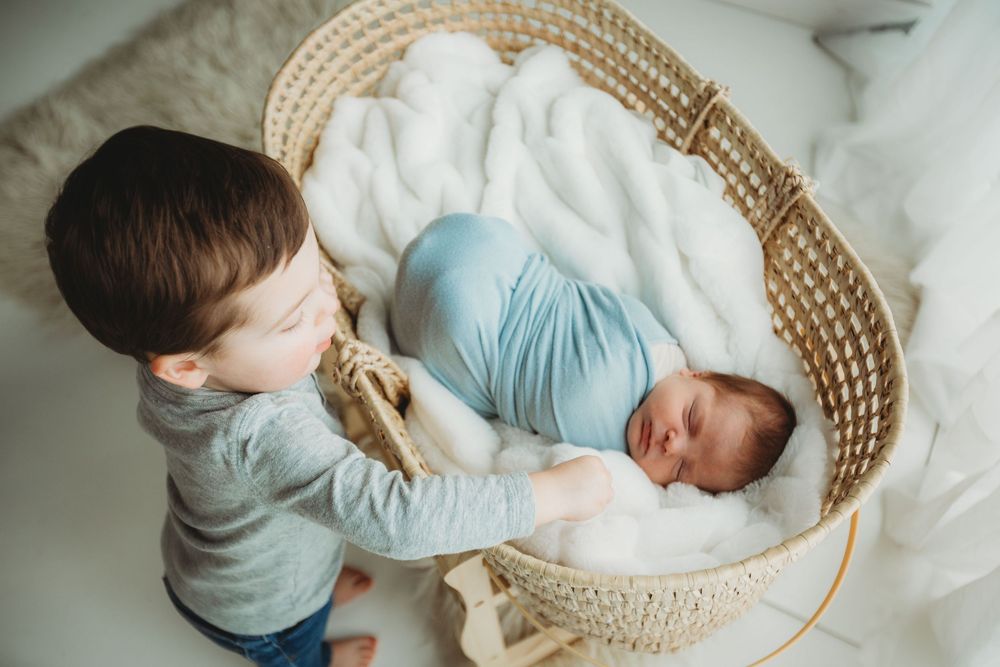 A series of photos showing a baby sleeping in a woven bassinet while being watched by a sibling.