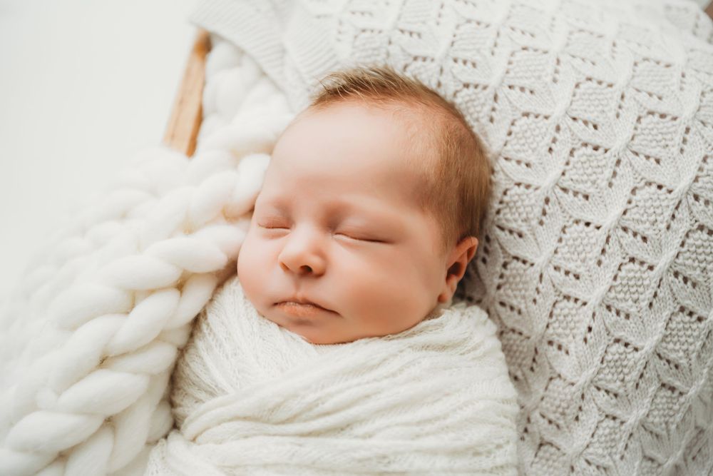 Sleeping baby wrapped in white blanket lying on textured knit blanket with peaceful expression.
