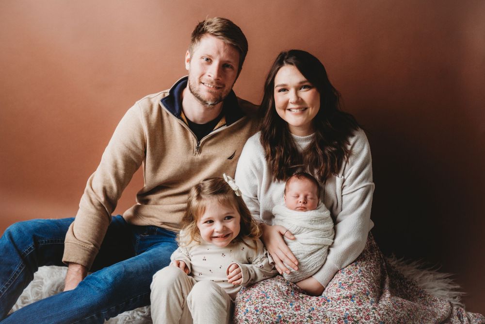 Family portrait session featuring parents and children in coordinating beige and neutral tones against warm brown backdrop.