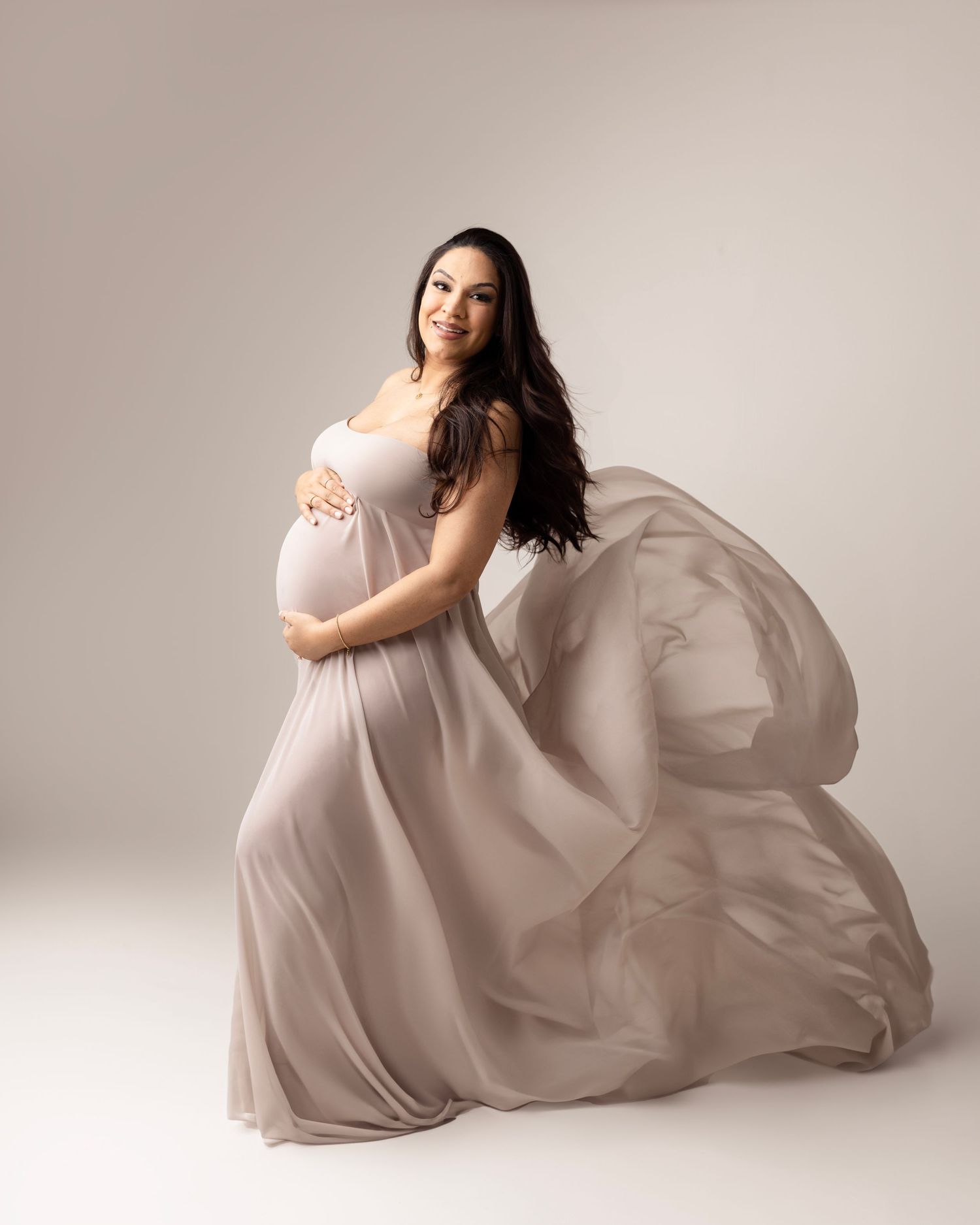 Artistic maternity photo series showing flowing beige fabric movement against neutral studio backdrop. Elizabeth Lang Photography Surrey