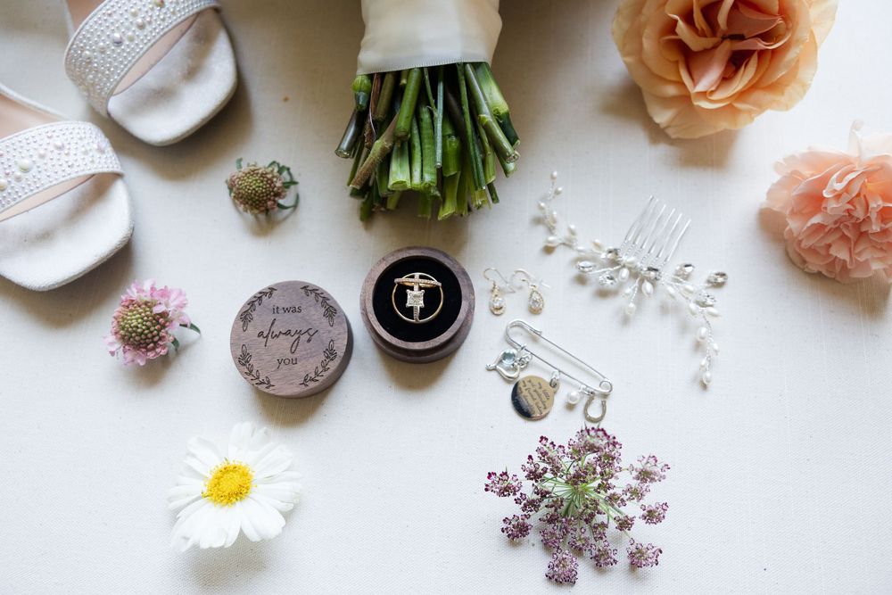 Flatlay of wedding details including flowers, ribbons and delicate accessories on white background.