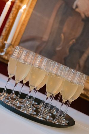 Row of champagne flutes filled with sparkling wine arranged on black serving trays at an elegant event.