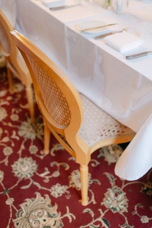 White chairs with decorative wooden backs arranged at tables with white linens on a floral patterned carpet.