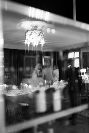 Black and white panoramic view of an elegant wedding reception venue with crystal chandeliers and formal table settings.