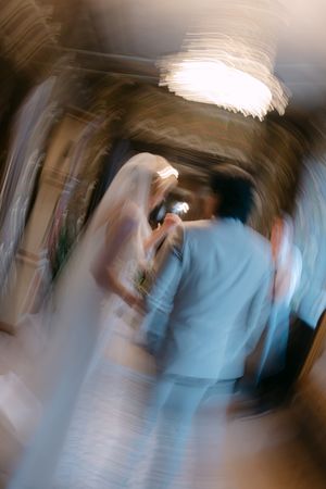 Motion blur photograph of a bride in white dress and someone in blue at a wedding ceremony.