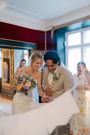 Wedding party laughing and celebrating in an elegant blue and burgundy room with large windows.