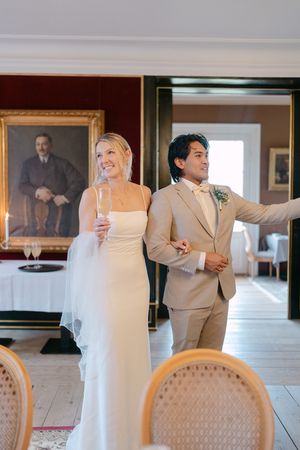 Wedding couple and guests mingling in an elegant dining room with cream-colored chairs and formal decor.