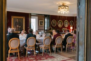 Elegant dining room with antique chairs, ornate chandeliers, and portrait-lined walls during a formal gathering.