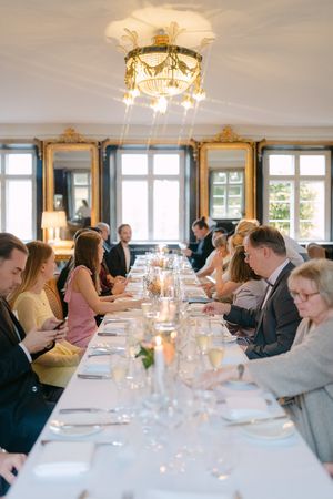Long formal dining table set with crystal glassware under an ornate chandelier in a room with gilded mirrors.