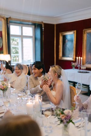 Wedding guests laugh together at an elegant reception table decorated with flowers and glassware.