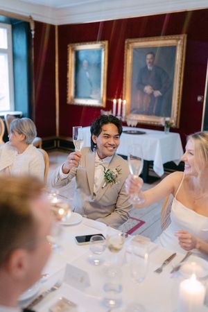 Wedding guests raise champagne glasses in a toast at an elegant dining table with white linens and candlelight.