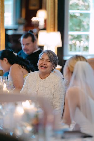Wedding guests share joyful laughter during an elegant indoor reception with warm lighting and white decor.