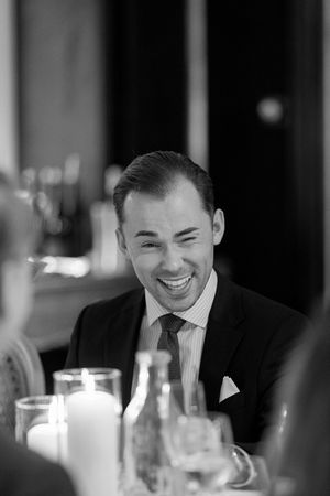 Black and white candid photo of guests laughing together at an elegant dinner party with candlelit table settings.