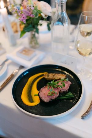 A fine dining plate featuring sliced medium-rare meat with a vibrant orange puree sauce on a black plate.