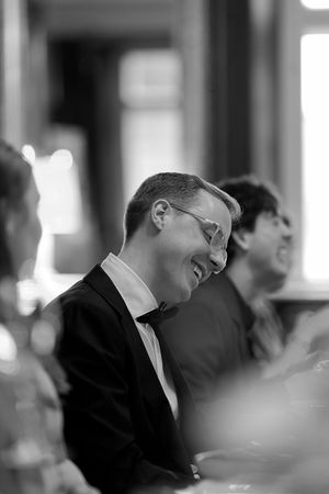 A black and white photo sequence shows someone in a suit laughing and tilting their head back in four progressive frames.