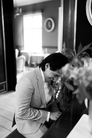 A person in a light gray suit jacket leans forward in a black and white photograph with soft window lighting.