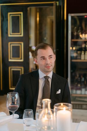 Elegant dining scene with lit candles and wine glasses on white tablecloth in upscale restaurant with dark paneled walls.